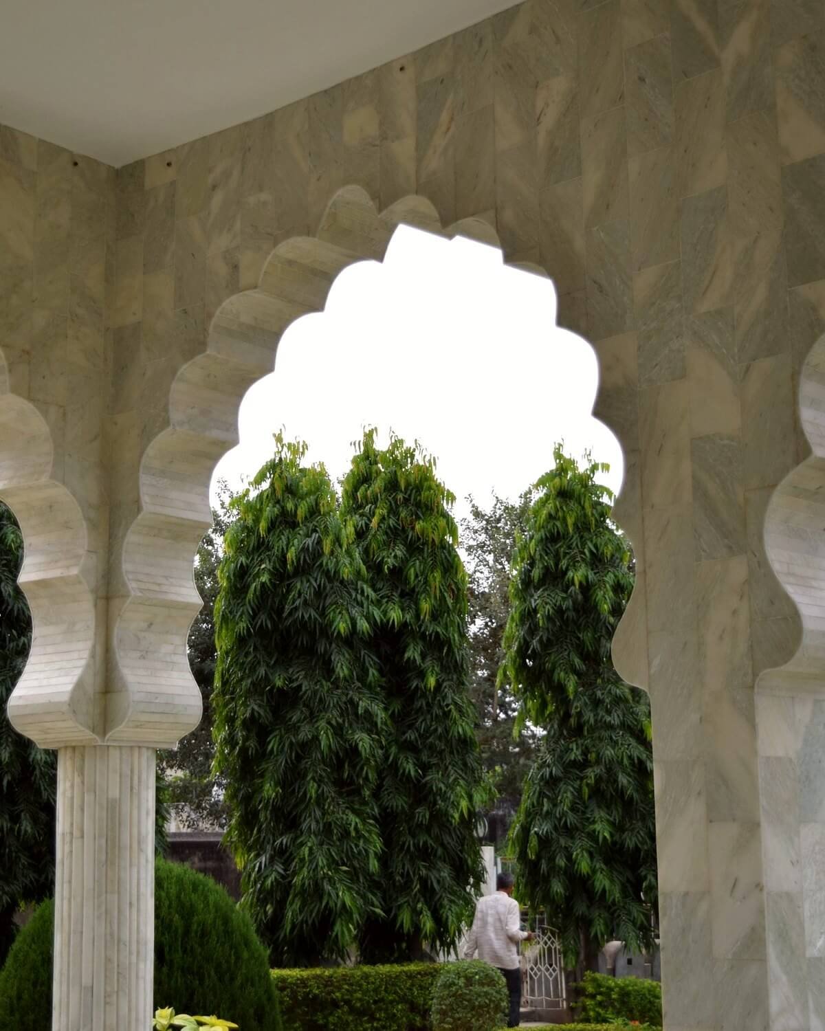 Carved Rajasthani arches framing columnar cypress trees in the garden